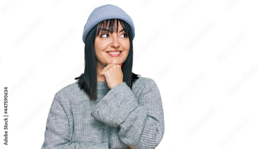 Young hispanic woman wearing cute wool cap with hand on chin thinking about question, pensive expression. smiling with thoughtful face. doubt concept.