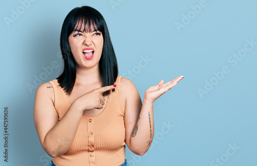 Young hispanic plus size woman pointing open palm with finger angry and mad screaming frustrated and furious, shouting with anger. rage and aggressive concept.