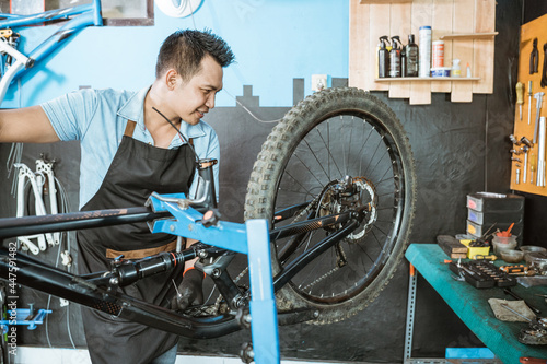 male bicycle mechanic in apron checking the function of freewhells while fixing problems on bicycles in a workshop