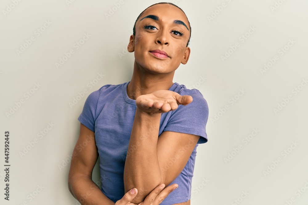 Hispanic man wearing make up and long hair wearing casual t shirt looking at the camera blowing a kiss with hand on air being lovely and sexy. love expression. Hispanic man wearing make up and long hair wearing casual t shirt looking at the camera blowing a kiss with hand on air being lovely and sexy. love expression.