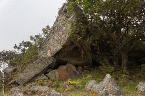 A Triangular extrange ancient monolith with a hole surrounded by trees into andean forest mountains