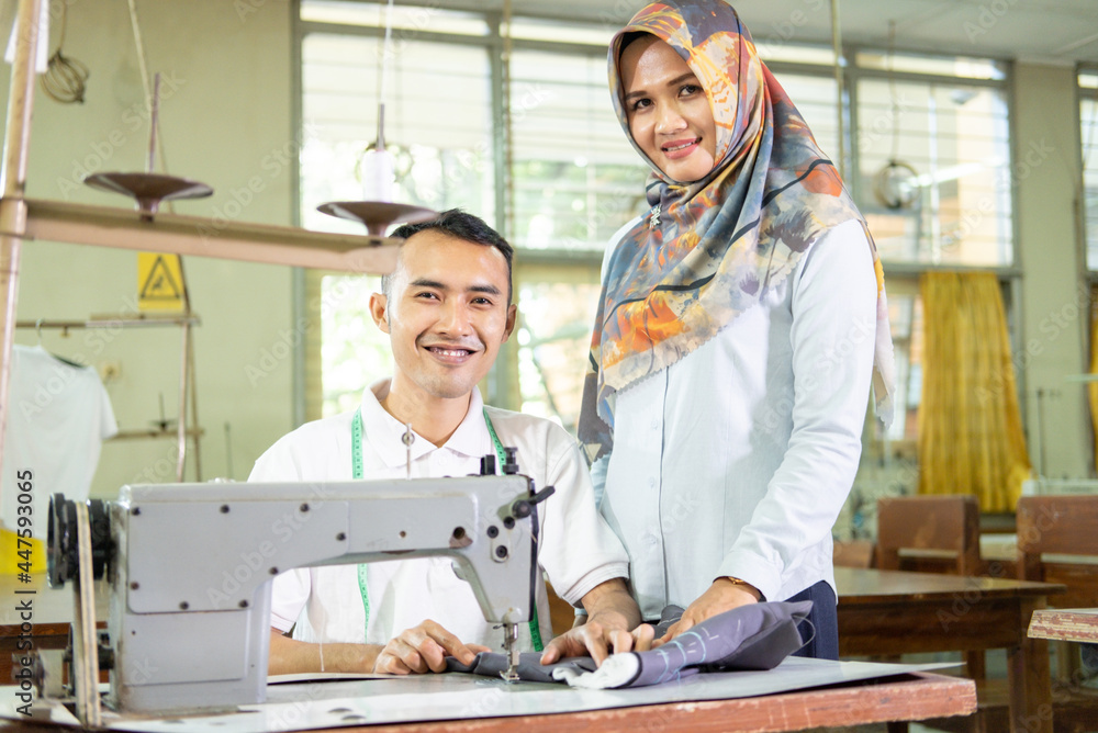 woman in headscarf, the owner of the garment convection, stand next to the working employee using the sewing machine in the production room woman in headscarf, the owner of the garment convection, stand next to the working employee using the sewing machine in the production room