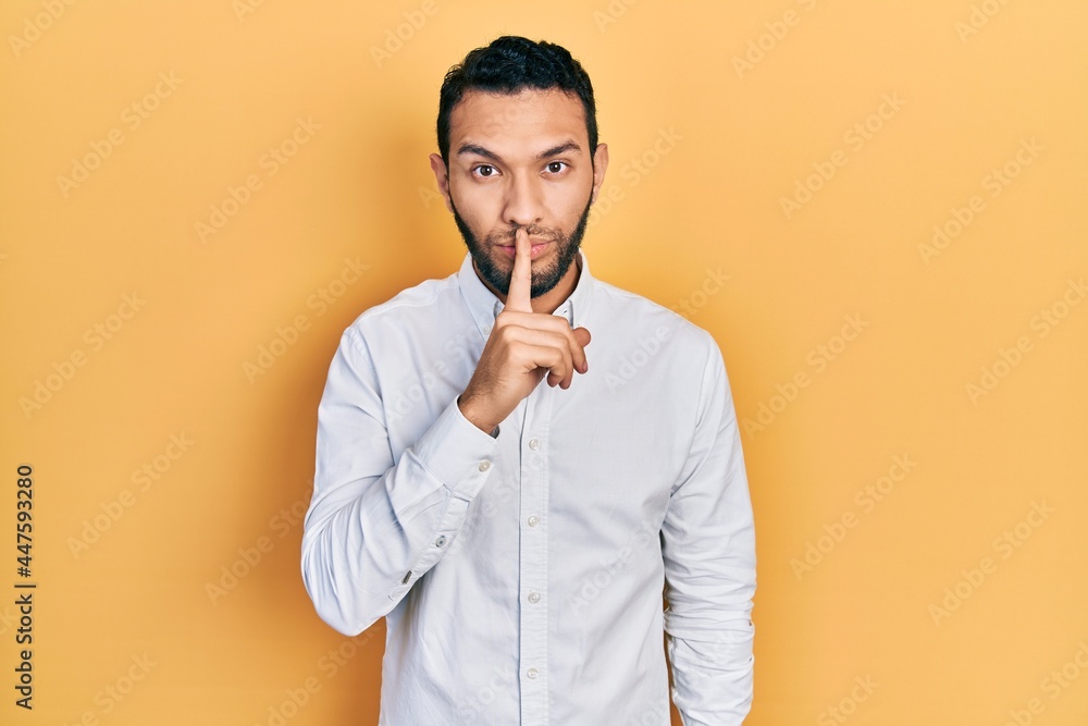 Hispanic man with beard wearing business shirt asking to be quiet with finger on lips. silence and secret concept. Hispanic man with beard wearing business shirt asking to be quiet with finger on lips. silence and secret concept.