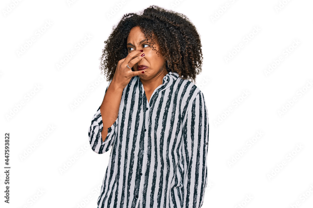 Young african american girl wearing casual clothes smelling something stinky and disgusting, intolerable smell, holding breath with fingers on nose. bad smell Young african american girl wearing casual clothes smelling something stinky and disgusting, intolerable smell, holding breath with fingers on nose. bad smell