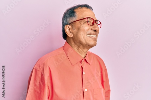 Middle age indian man wearing casual clothes and glasses looking away to side with smile on face, natural expression. laughing confident.
