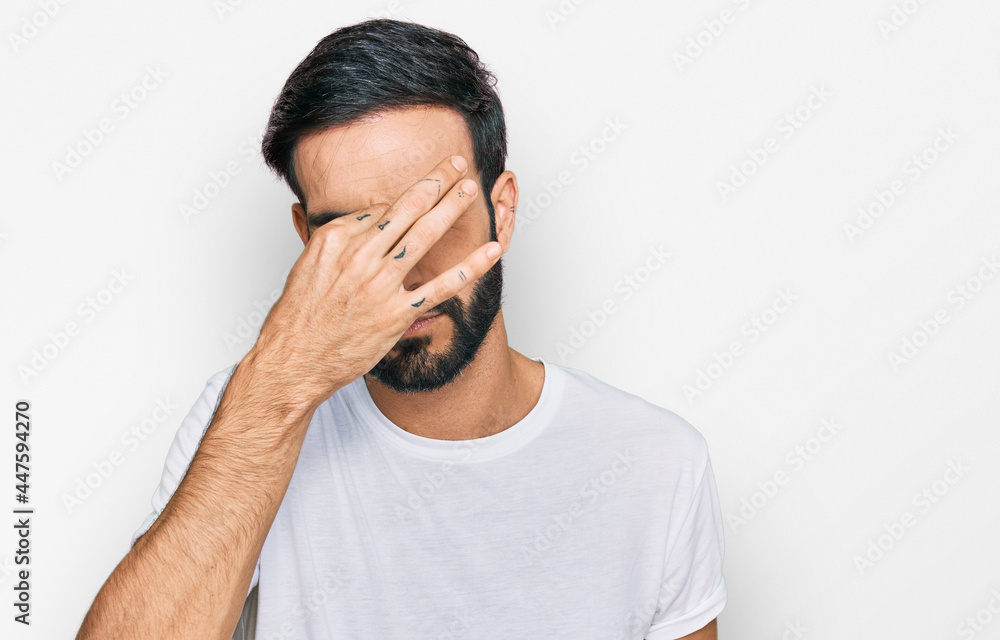 Young hispanic man wearing casual white t shirt tired rubbing nose and eyes feeling fatigue and headache. stress and frustration concept. Young hispanic man wearing casual white t shirt tired rubbing nose and eyes feeling fatigue and headache. stress and frustration concept.