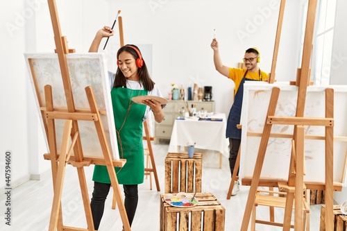 Young hispanic couple smiling happy listening to music and drawing at art studio.