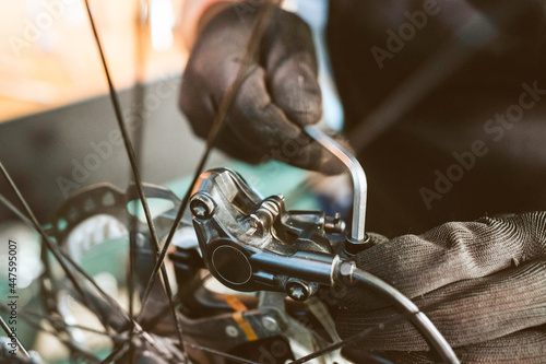 hands of a bicycle mechanic wearing gloves using an allen key to tighten bolts while working in a workshop photo