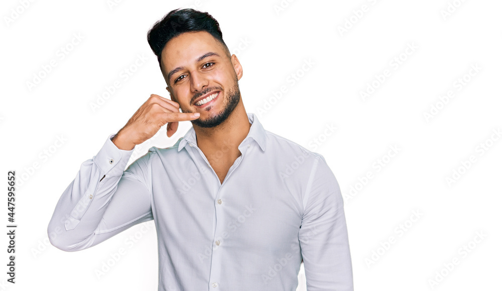Young arab man wearing casual clothes smiling doing phone gesture with hand and fingers like talking on the telephone. communicating concepts. Young arab man wearing casual clothes smiling doing phone gesture with hand and fingers like talking on the telephone. communicating concepts.