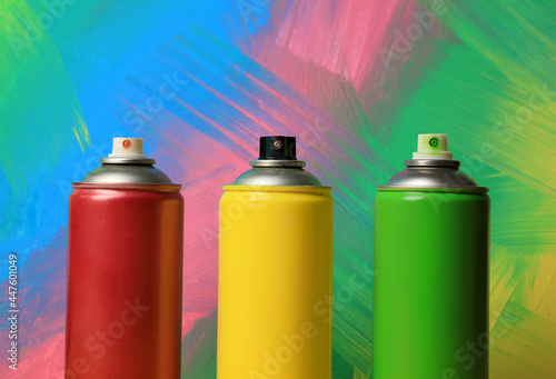 Cans of different spray paints on color background, closeup. Graffiti supplies