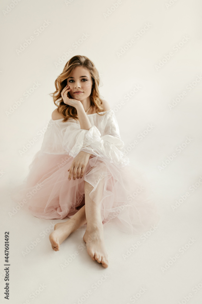Charming young lady with blonde wavy hair in stylish light blouse and long pink skirt posing on white isolated background.. Charming young lady with blonde wavy hair in stylish light blouse and long pink skirt posing on white isolated background..