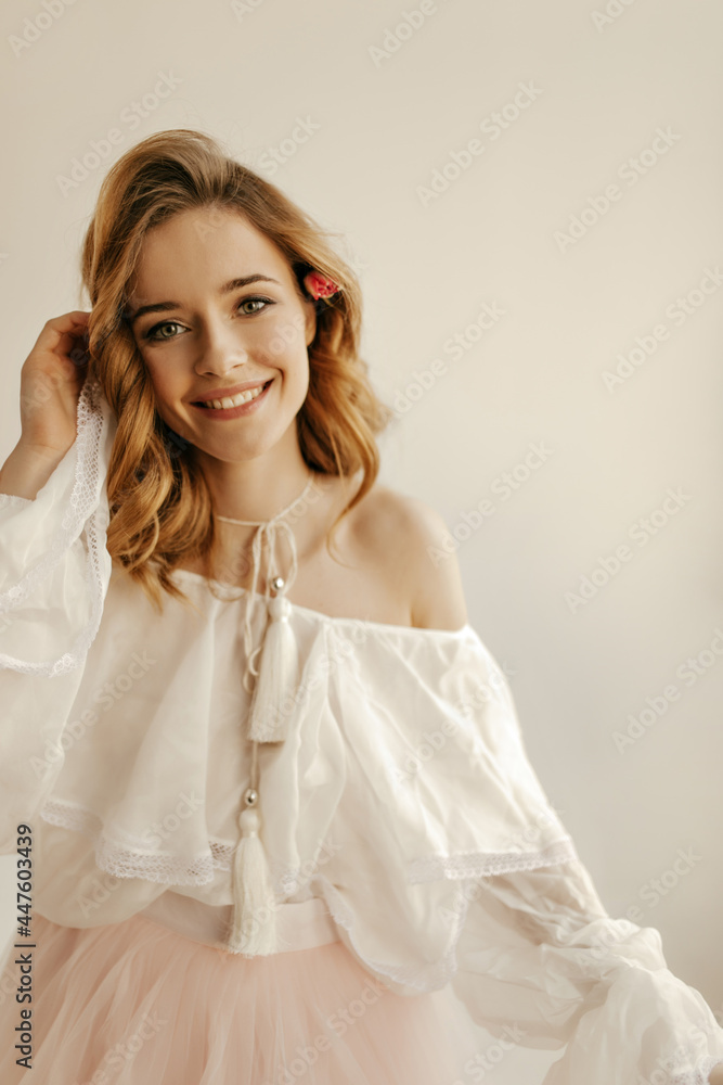 Cheerful lovely girl with curly blond hairstyle in white shirt with long sleeves looking into camera and smiling on isolated background.. Cheerful lovely girl with curly blond hairstyle in white shirt with long sleeves looking into camera and smiling on isolated background..