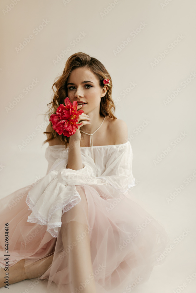 Beautiful curly haired woman in white blouse and pink long skirt looking into camera with flowers. Modern girl posing with tulip in her hair.. Beautiful curly haired woman in white blouse and pink long skirt looking into camera with flowers. Modern girl posing with tulip in her hair..