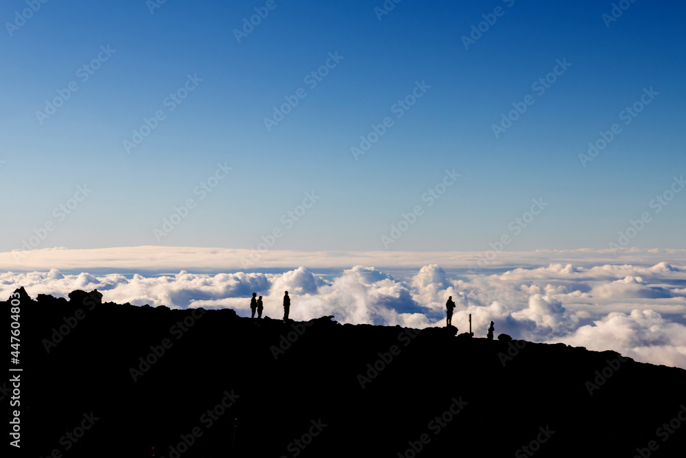 Silhouette of a group of people standing on the summit of the Haleakalā volcano, looking down on the clouds.