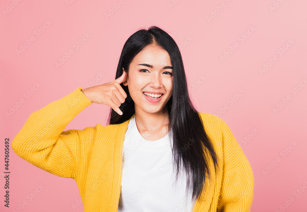 Portrait Asian beautiful young woman smiling doing phone gesture with hand and fingers like talking on the telephone, studio shot isolated pink background, Thai female communicating gesture