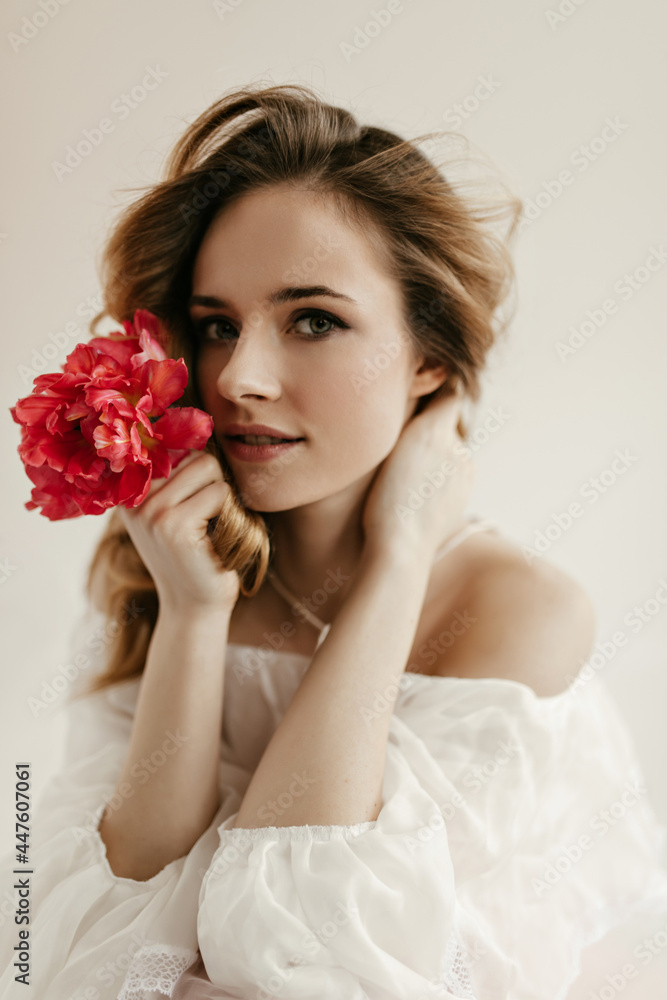 Pretty wavy girl in stylish shirt with long sleeves looking into camera. Blue-eyed woman posing with red peony on isolated background.. Pretty wavy girl in stylish shirt with long sleeves looking into camera. Blue-eyed woman posing with red peony on isolated background..
