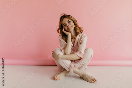Tender curly blond haired woman in pink lovely suit posing and smiling on isolated background. Girl in light outfit looking into camera..