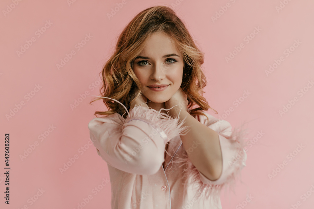 Pretty young woman with curly blond hair in fashionable pink outfit looking into camera. Lady with tender makeup posing.. Pretty young woman with curly blond hair in fashionable pink outfit looking into camera. Lady with tender makeup posing..