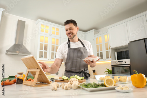 Happy man making dinner while watching online cooking course via tablet in kitchen
