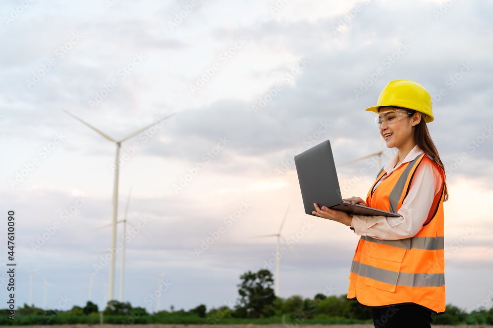 female engineer working with laptop computer against wind turbine farm female engineer working with laptop computer against wind turbine farm