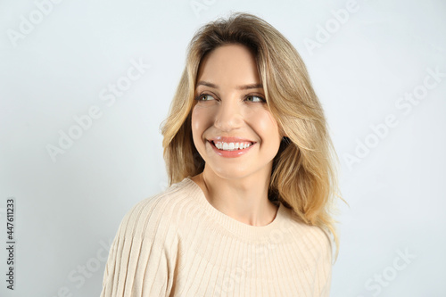 Portrait of happy young woman with beautiful blonde hair and charming smile on light background © New Africa