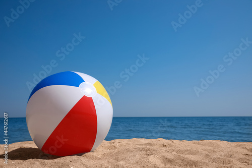 Colorful inflatable ball on sandy beach. Space for text