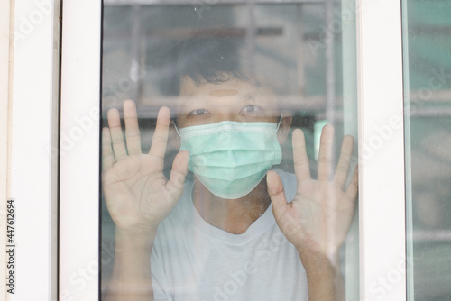 Sick man of corona virus looking through the window and wearing mask protection and recovery from the illness in home. Quarantine. Patient isolated to prevent infection. Pandemia.