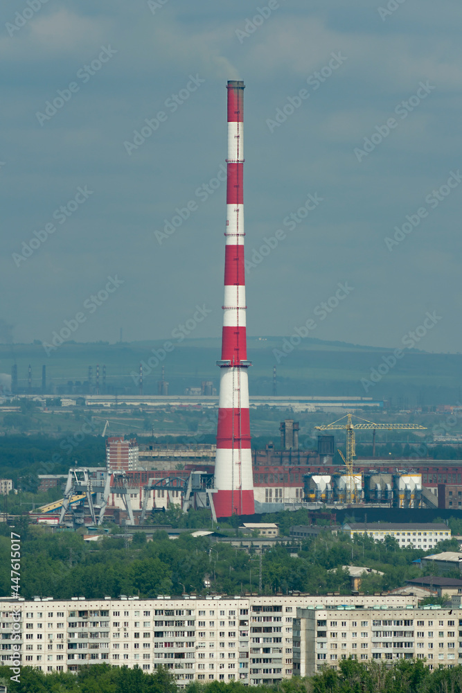 A huge red-white brick chimney in the center of an industrial city.