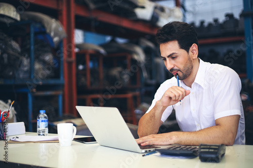 Businessman using laptop computer working or checking stock in warehouse factory, entrepreneurship or business owner concept