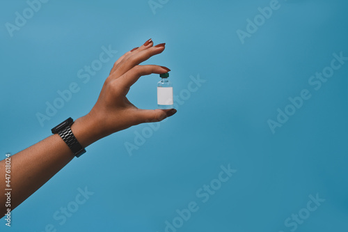 Woman holding bottle of vaccine on blue background. Vaccine Concept.