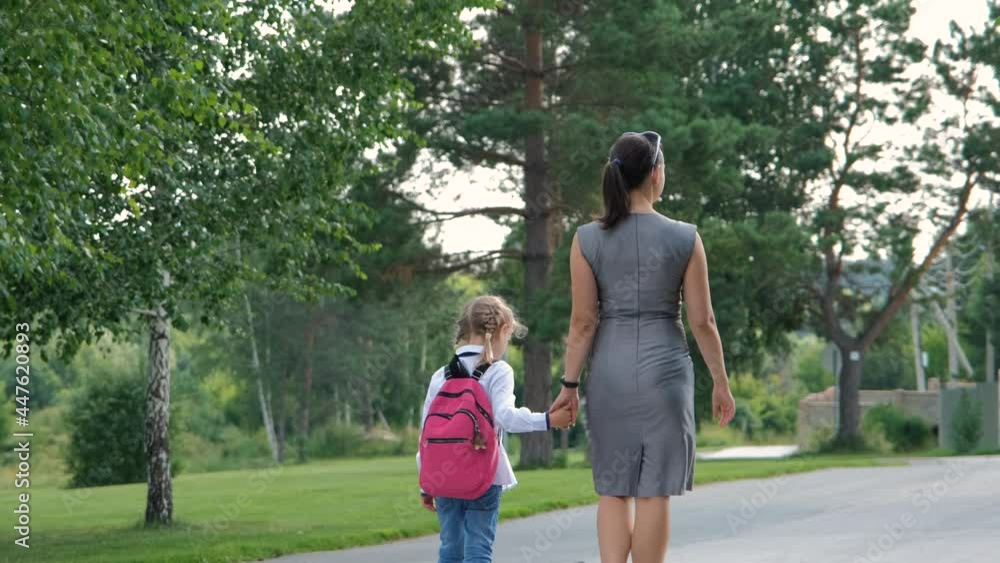 Mother Leads her Cute Little Daughter at School, Holding Hands Together. Back View. First Day at School Concept Mother Leads her Cute Little Daughter at School, Holding Hands Together. Back View. First Day at School Concept