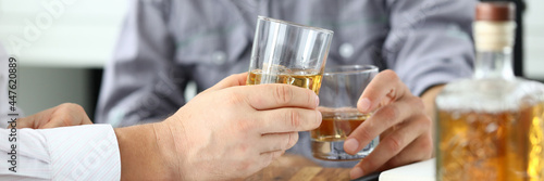 Two business men drinking cognac from glasses at workplace closeup