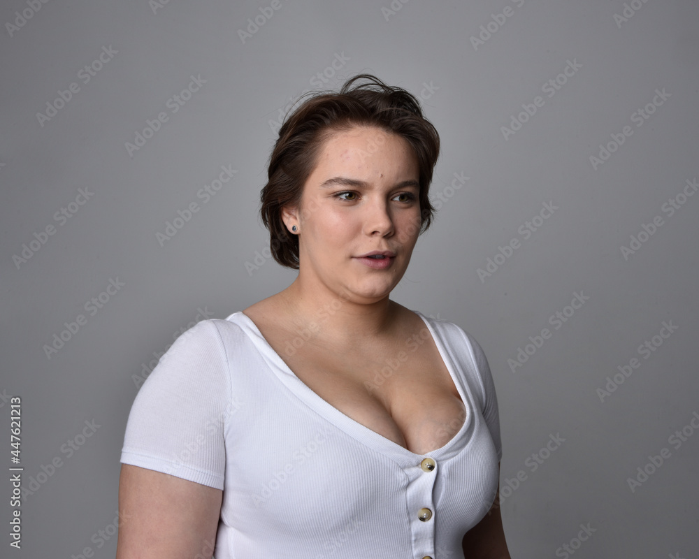 Close up portrait of young plus sized woman with short brunette hair, wearing a white shirt, with over the top emotional facial expressions against a light studio background. Close up portrait of young plus sized woman with short brunette hair, wearing a white shirt, with over the top emotional facial expressions against a light studio background.