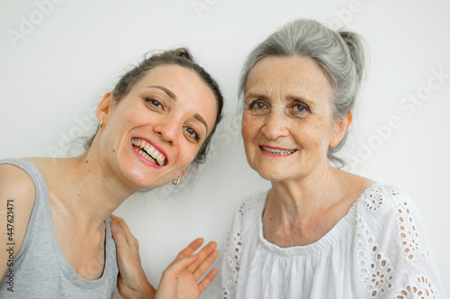 Happy senior mother is hugging her adult daughter, the women are laughing together, sincere family of different age generations having fun on white background, mothers day.