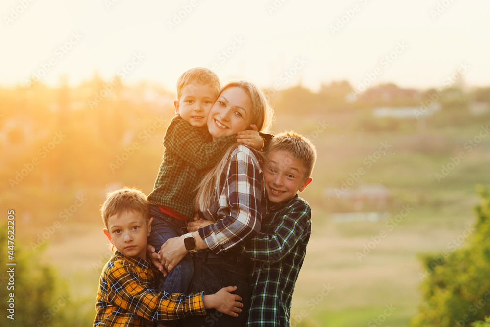 Fototapeta premium Happy mother and her three son are playing at sunset time. Friendly family concept. To explore nature in evening on sunshine warm summer day. Spend time together