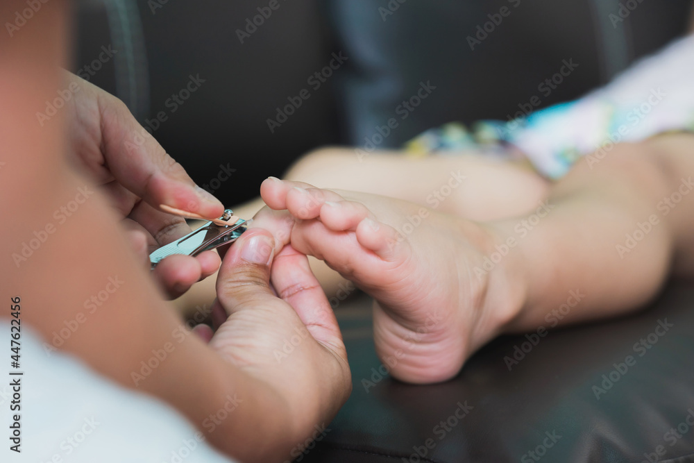 Closeup hand's mom holding nail clippers, cutting toenails  to daughter girl. Child lying down on  sofa. Baby aged 4-5 years old.
