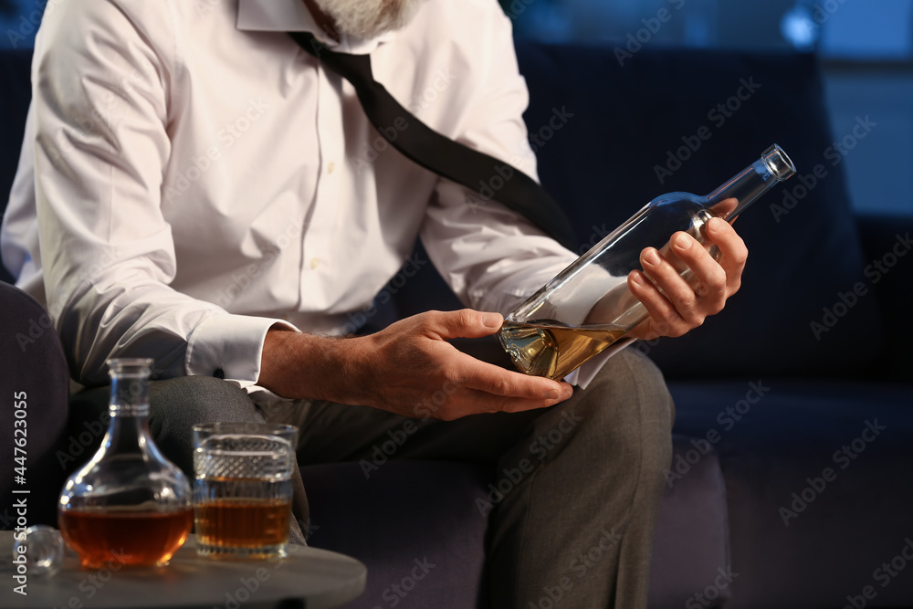 Senior man with bottle of drink late in evening at home