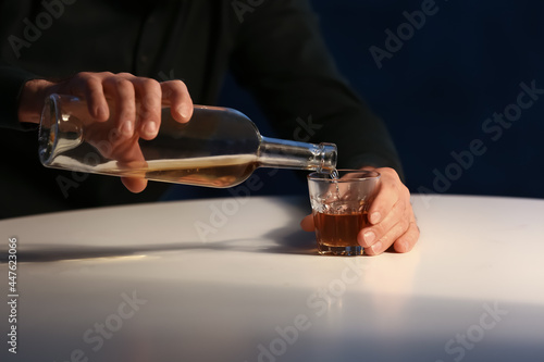 Senior man pouring drink in glass in kitchen at night, closeup