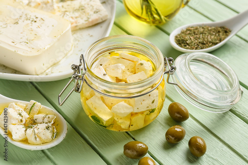 Glass jar with tasty feta cheese, oil, olives on color wooden background, closeup