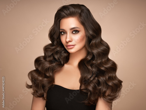Brunette girl with perfect makeup. Smiling beautiful model woman with long curly hairstyle. Care and beauty hair products