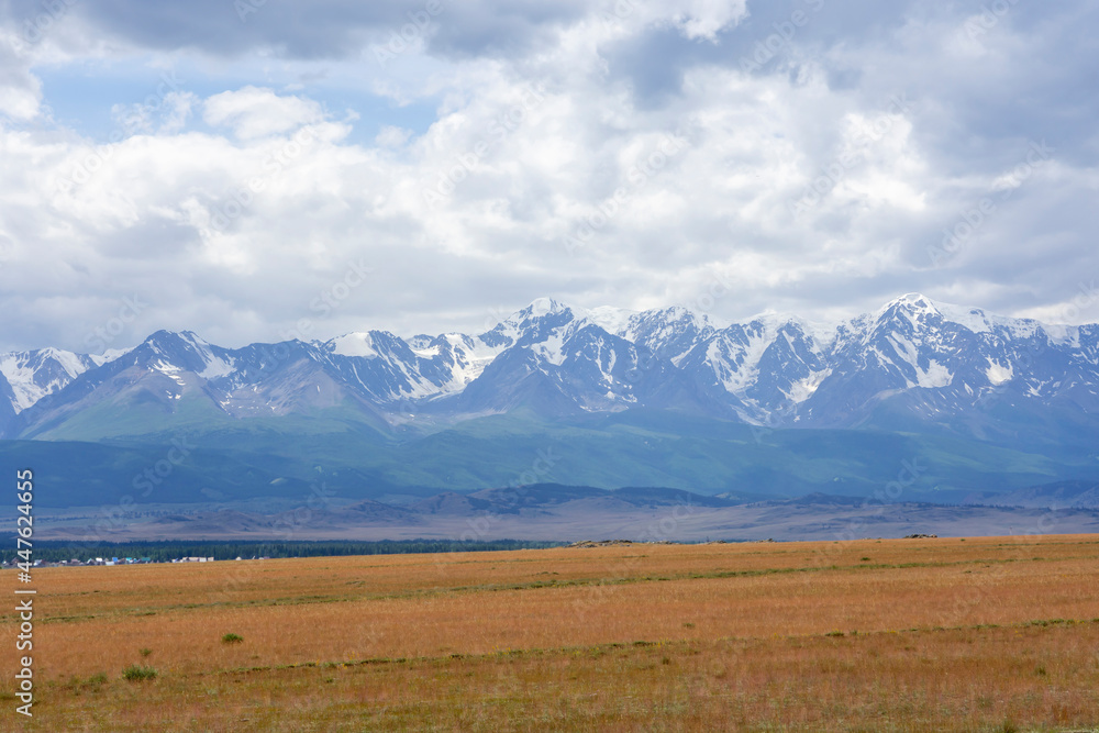 snowy peaks of mountains and steppe on a background of cloudy sky snowy peaks of mountains and steppe on a background of cloudy sky