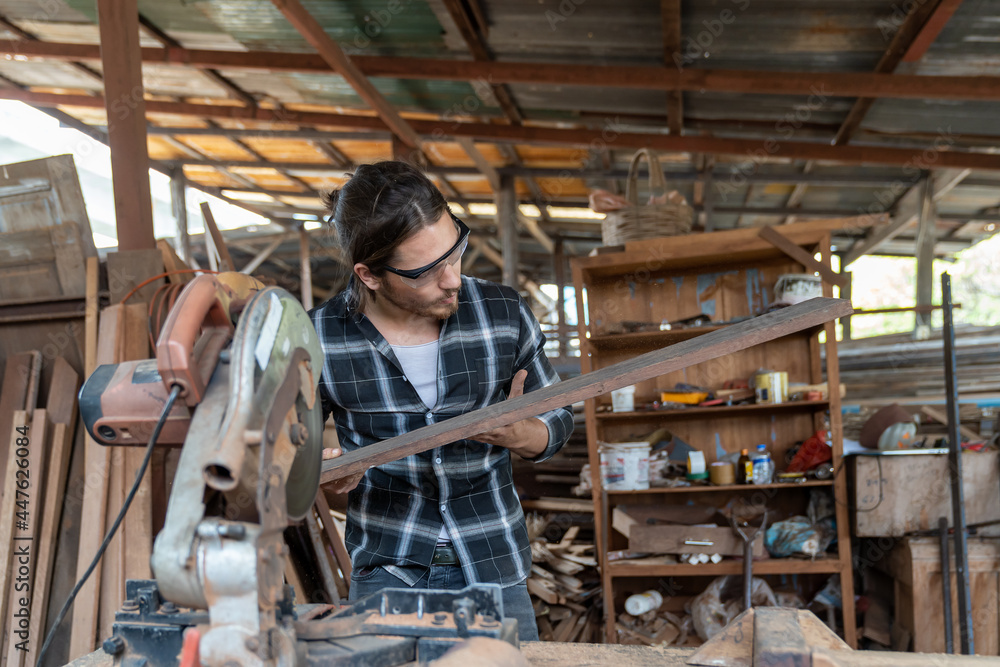 Male carpenter using circular saw cutting piece of wood and wearing safety goggles at woodwork workshop. Male woodworker working at work. Professional male craftsman