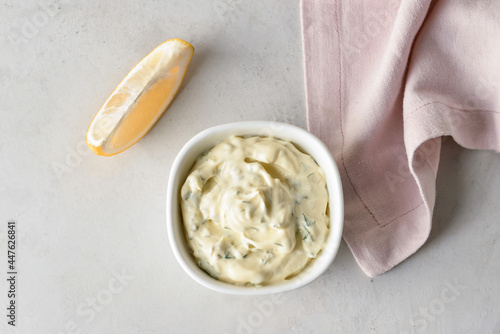 Bowl with tasty tartare sauce and lemon on light background, closeup