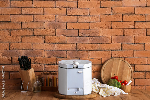 Modern deep fryer, kitchen utensils and products on table near brick wall