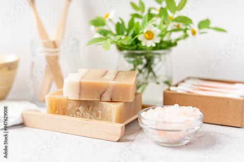 Natural bathroom and home spa tools. Zero waste sustainable lifestyle concept. Bamboo toothbrush, natural soap bar in wooden soap dish, cotton pads, flowers, cotton swabs. White background, copy space