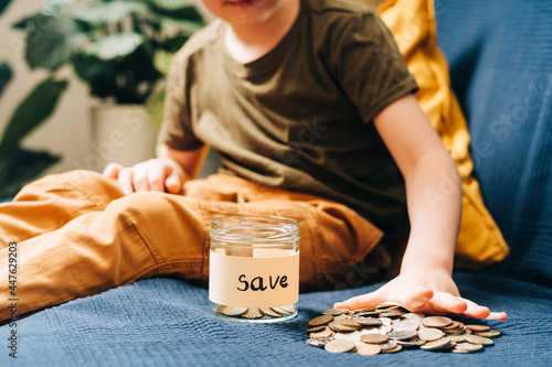 Close up of Little child kid boy hands grabbing and putting stack coins in to glass jar with save label. Donation, saving money, charity, family finance plan concept.