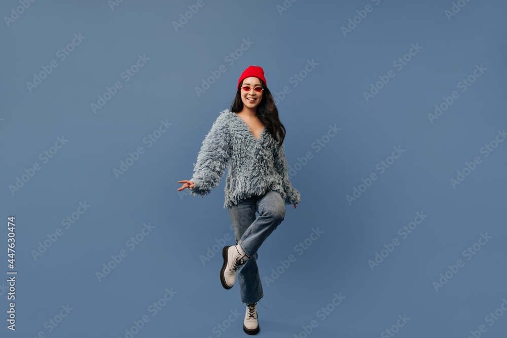 Joyful modern lady with red sunglasses in fashionable blue outfit and light cool shoes dancing and looking into camera on isolated backdrop.. Joyful modern lady with red sunglasses in fashionable blue outfit and light cool shoes dancing and looking into camera on isolated backdrop..