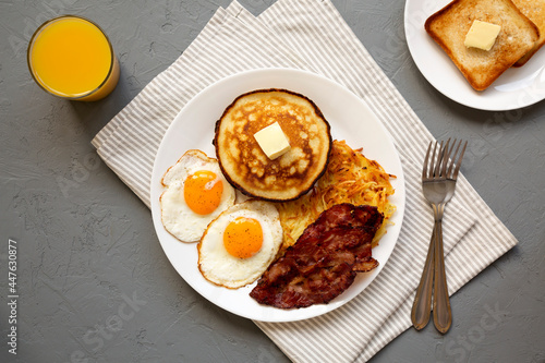 Full American Breakfast with Bacon, Hash Browns, Eggs and Pancakes on a plate on a gray surface, top view. Flat lay, overhead, from above.