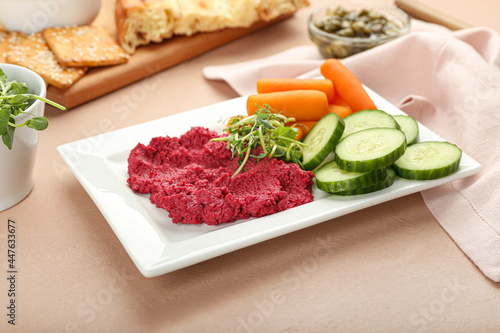 Plate with tasty beet hummus, carrots and cucumbers on color background