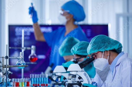 Group of female researchers or scientists wearing protective hygiene masks and medical uniforms working with microscopes and test tube in laboratory studying and analyzing about coronavirus situation.